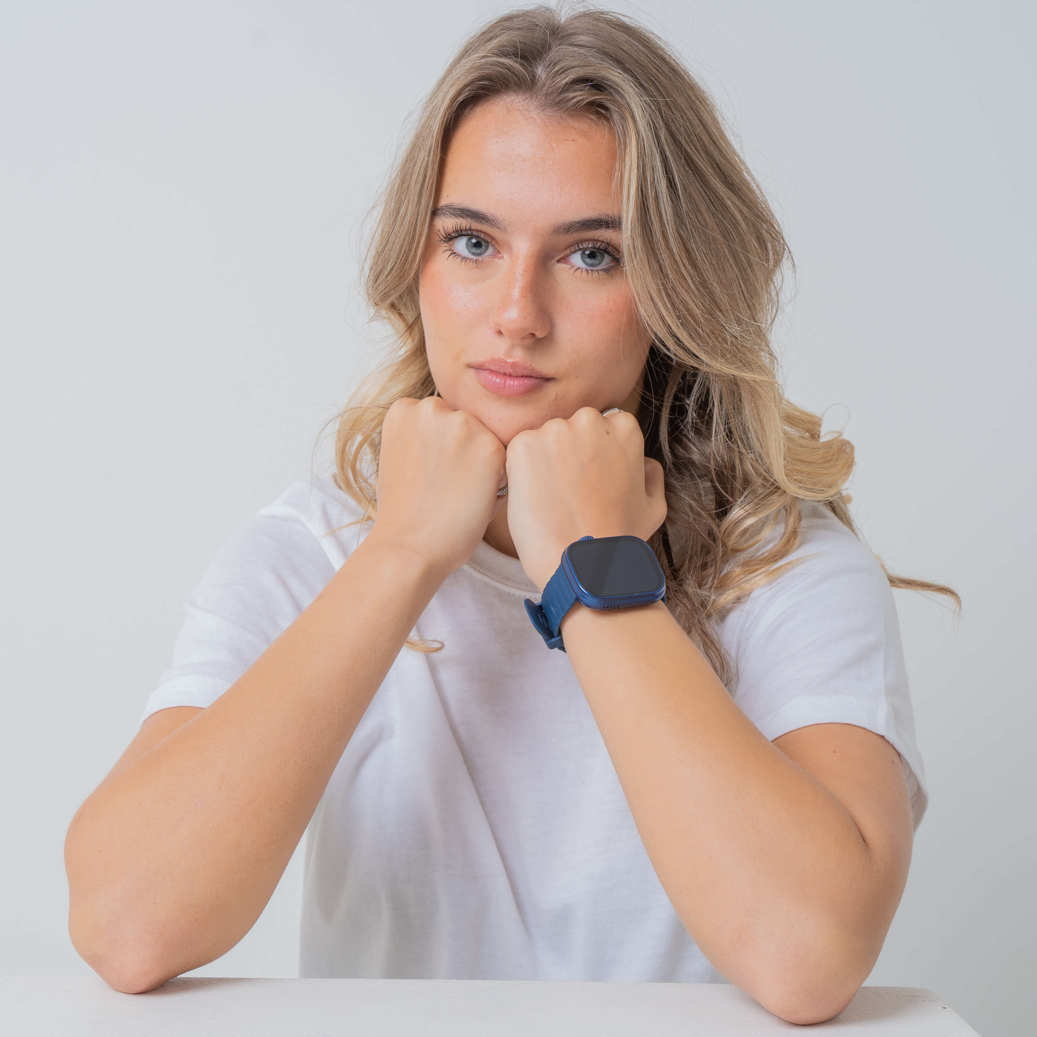 Blonde model wearing blue lynx smartwatch in plain background.