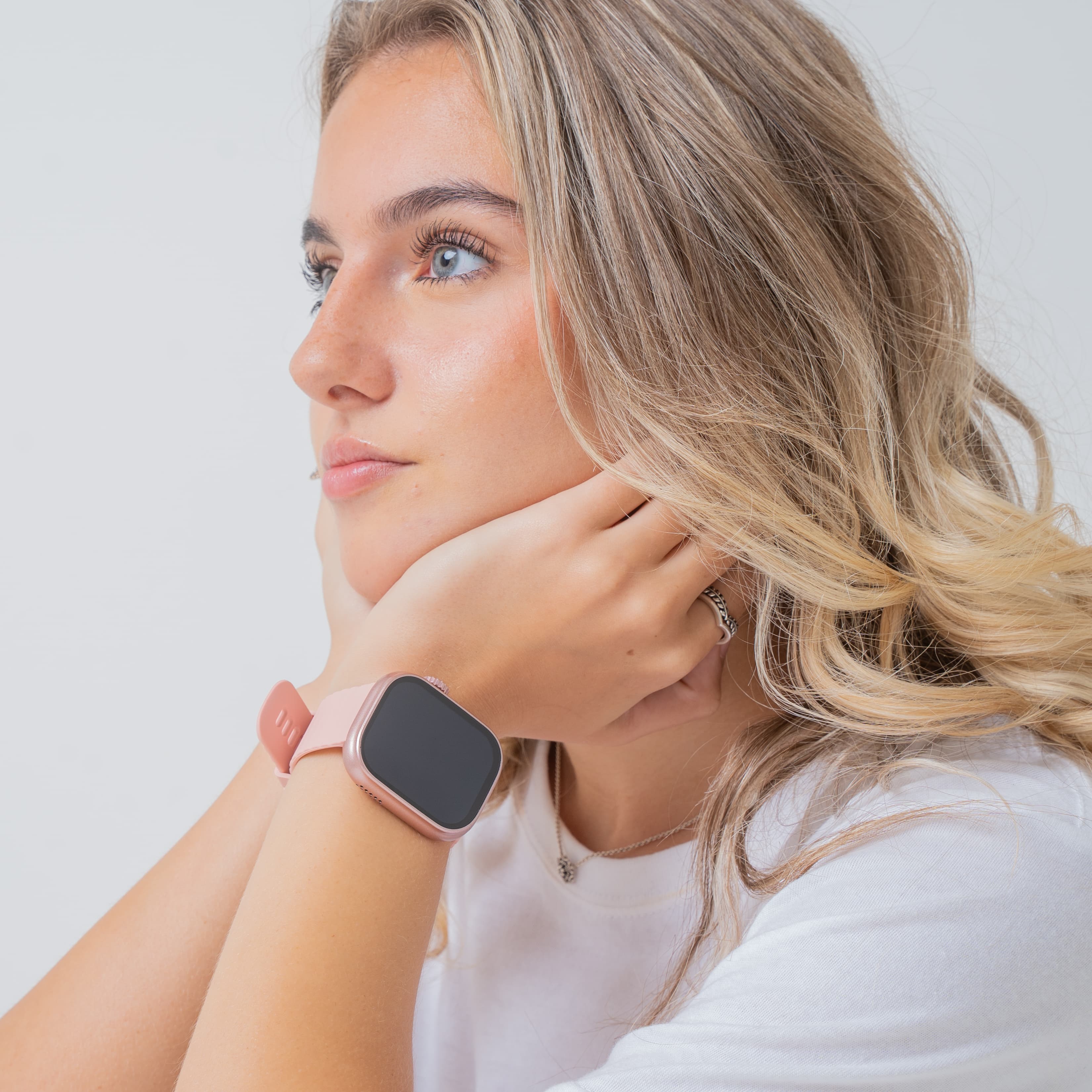 Blonde model wearing pink lynx smartwatch in plain background.